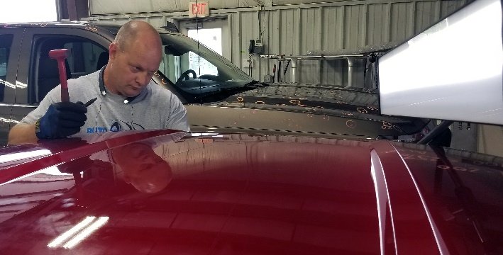 auto body tech applying paintless dent repair technique to fix dents in hood of a red car