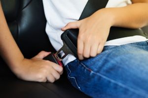 a child putting on their seat belt inside a vehicle