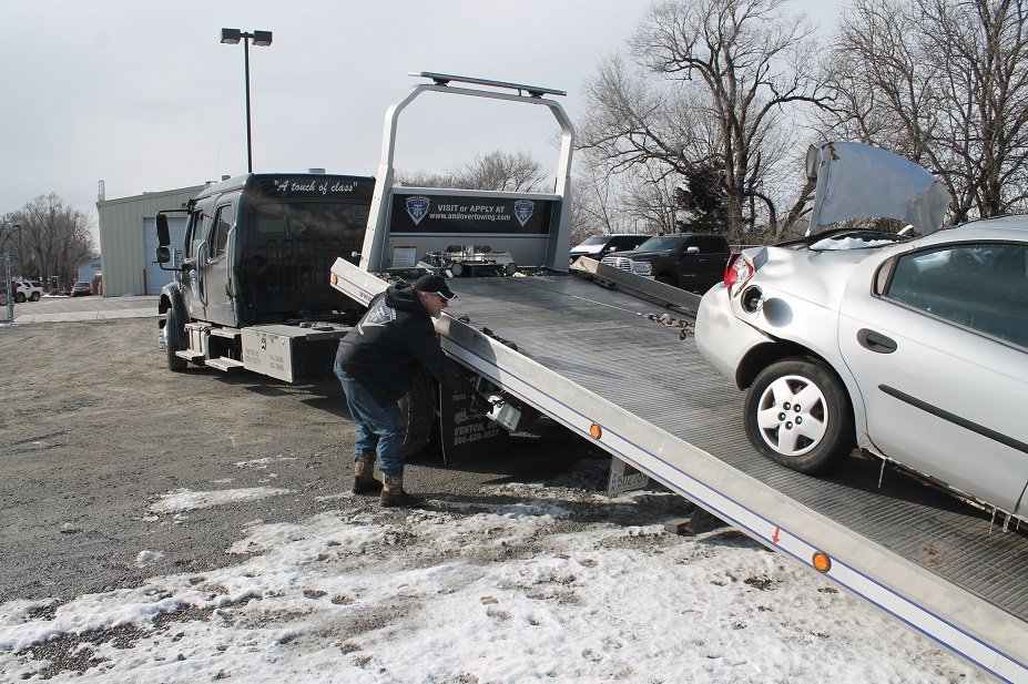 Tow truck carrying damaged car. Towing services from Collision Center of Andover, serving entire Wichita area.