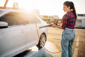 woman cleaning her white car with a hose because a dirty vehicle is a bad driver habit
